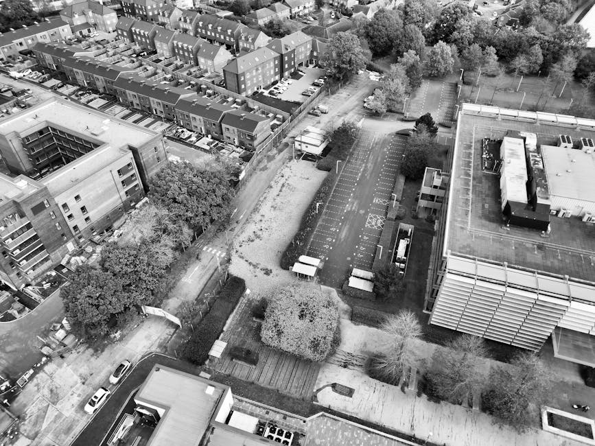 An aerial view of an urban area showing residential buildings with multiple floors, constructed from brick and concrete, featuring flat roofs and small balconies. Interspersed among the buildings are